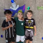 Alunos fantasiados posam diante do painel de máscaras de carnaval do colégio