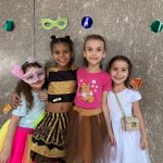 Alunos fantasiados posam diante do painel de máscaras de carnaval do colégio