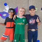Alunos fantasiados posam diante do painel de máscaras de carnaval do colégio