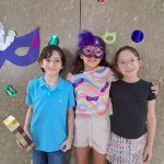 Alunos fantasiados posam diante do painel de máscaras de carnaval do colégio