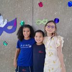 Alunos fantasiados posam diante do painel de máscaras de carnaval do colégio