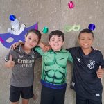 Alunos fantasiados posam diante do painel de máscaras de carnaval do colégio