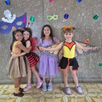 Alunos fantasiados posam diante do painel de máscaras de carnaval do colégio