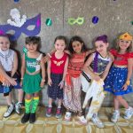 Alunos fantasiados posam diante do painel de máscaras de carnaval do colégio