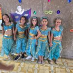 Cinco meninas fantasiadas com traje azul diante do painel de máscaras no Carnaval do Coração