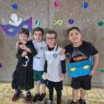 Alunos fantasiados posam diante do painel de máscaras de carnaval do colégio