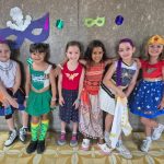 Alunos fantasiados posam diante do painel de máscaras de carnaval do colégio