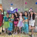 Alunos fantasiados posam diante do painel de máscaras de carnaval do colégio