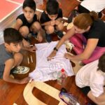 Alunos e professora decorando no chão da sala a camiseta branca da homenagem Mamãe Camisa 10