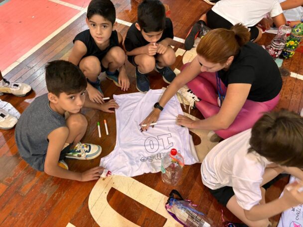 Alunos e professora decorando no chão da sala a camiseta branca da homenagem Mamãe Camisa 10
